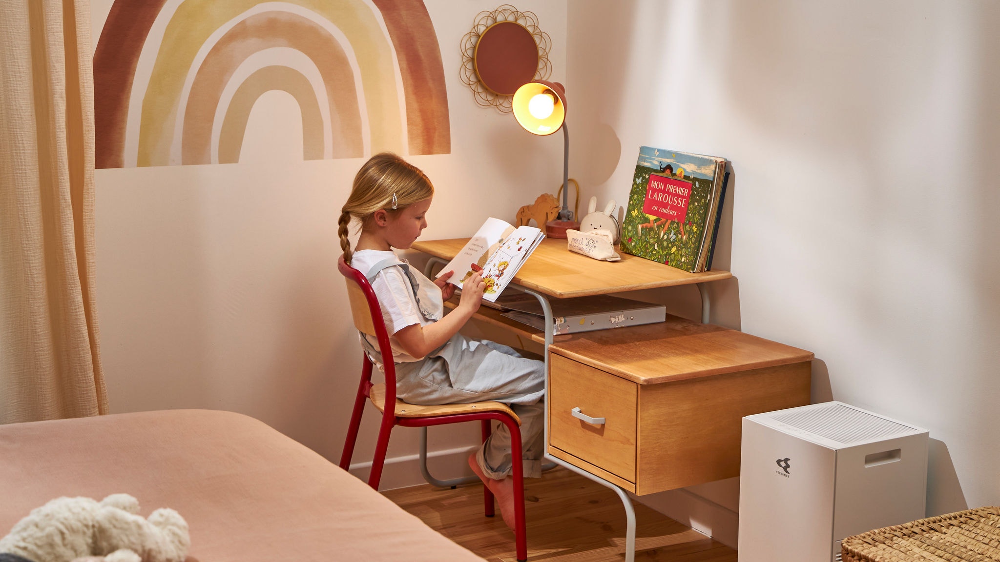 Niña leyendo un libro infantil disfrutando de aire de calidad gracias al purificador de aire situado junto a su escritorio