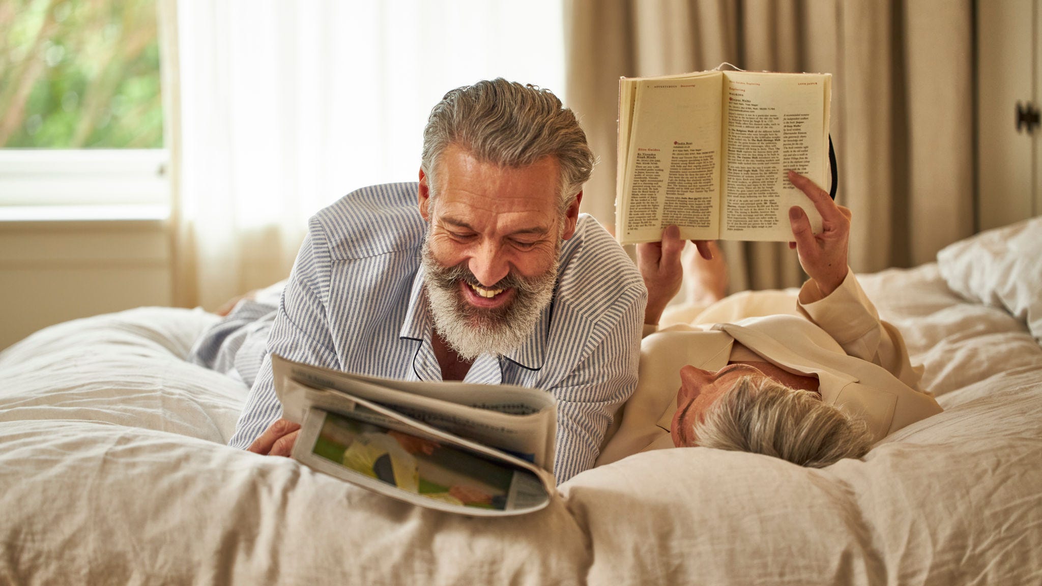 Pareja de mediana edad leyendo y relajándose en su cama mientras disfruta de una buena calidad del aire interior