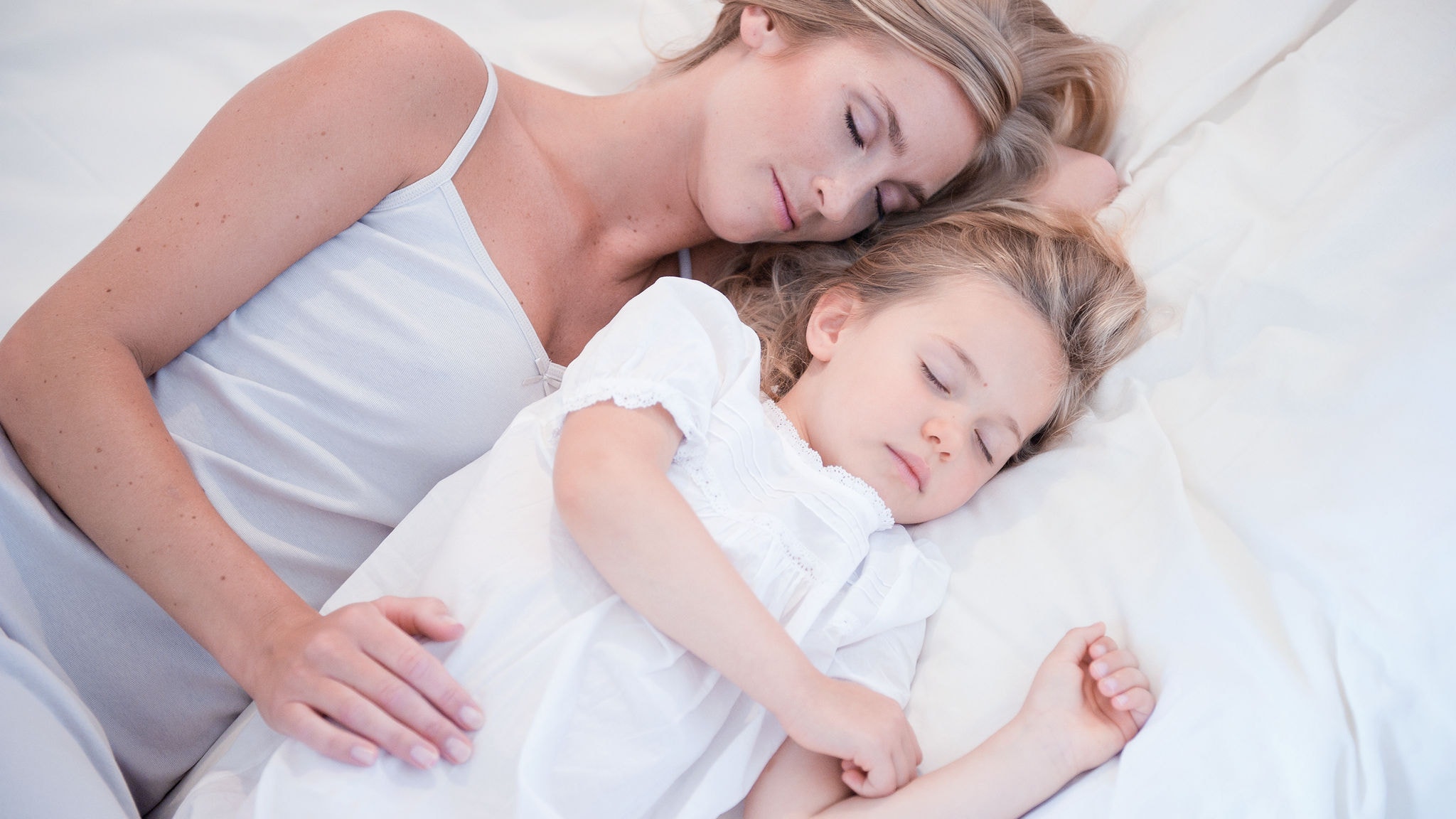 Madre e hija pequeña durmiendo juntas y disfrutando del aire limpio en una cama blanca