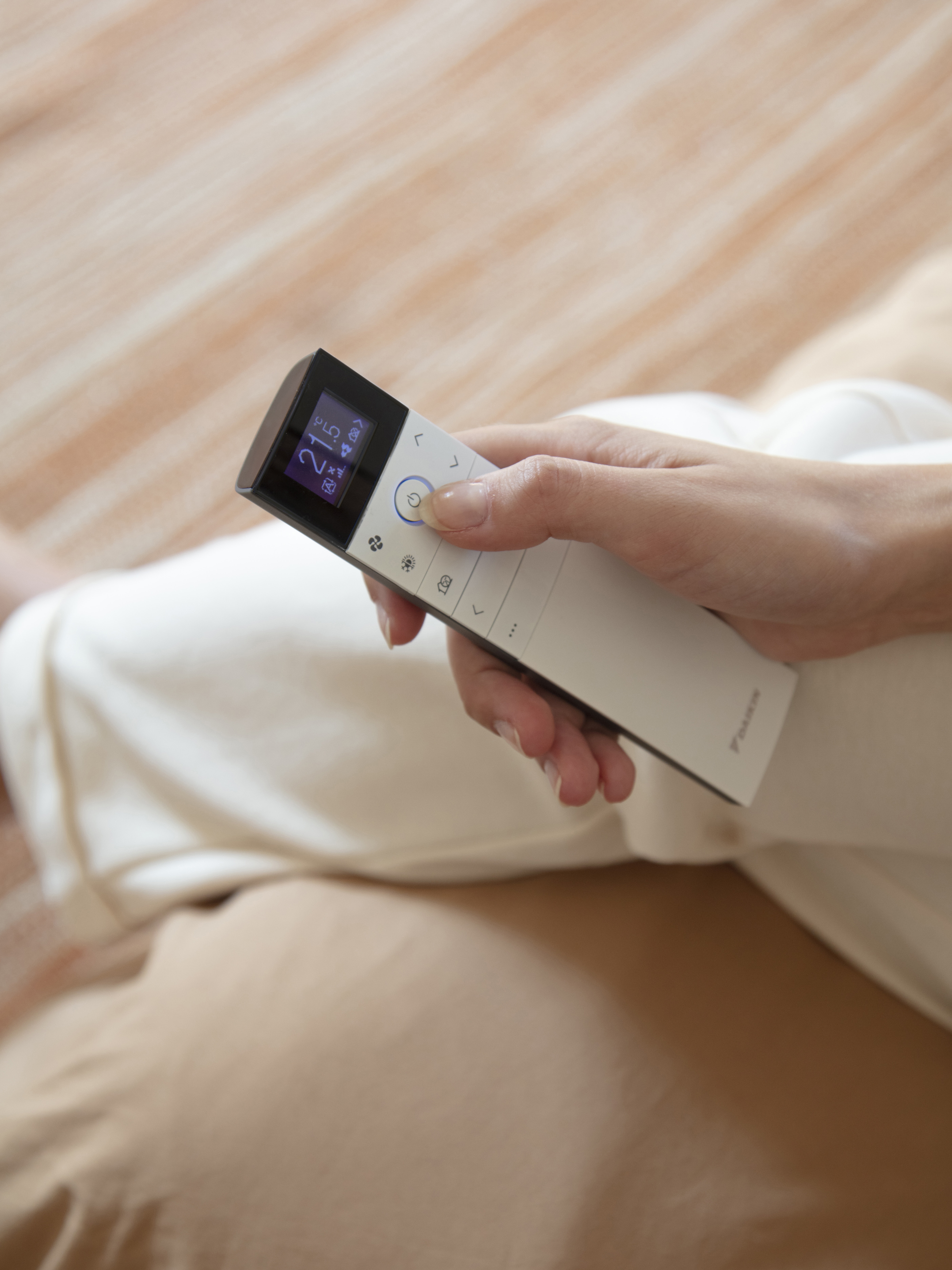 Una mujer controla la tecnología de climatización con un mando a distancia desde el sofá
