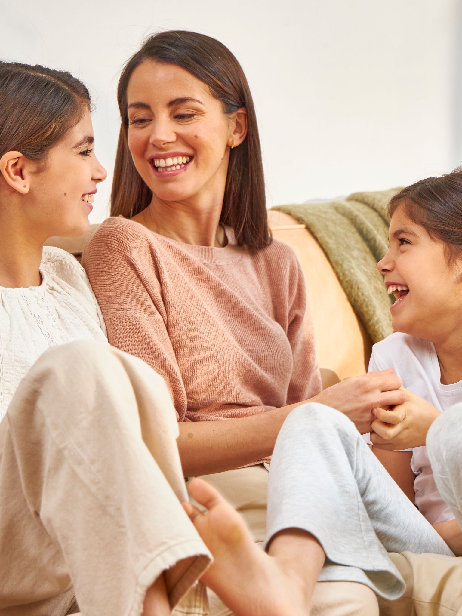 Madre y dos hijas riendo sentadas en el sofá