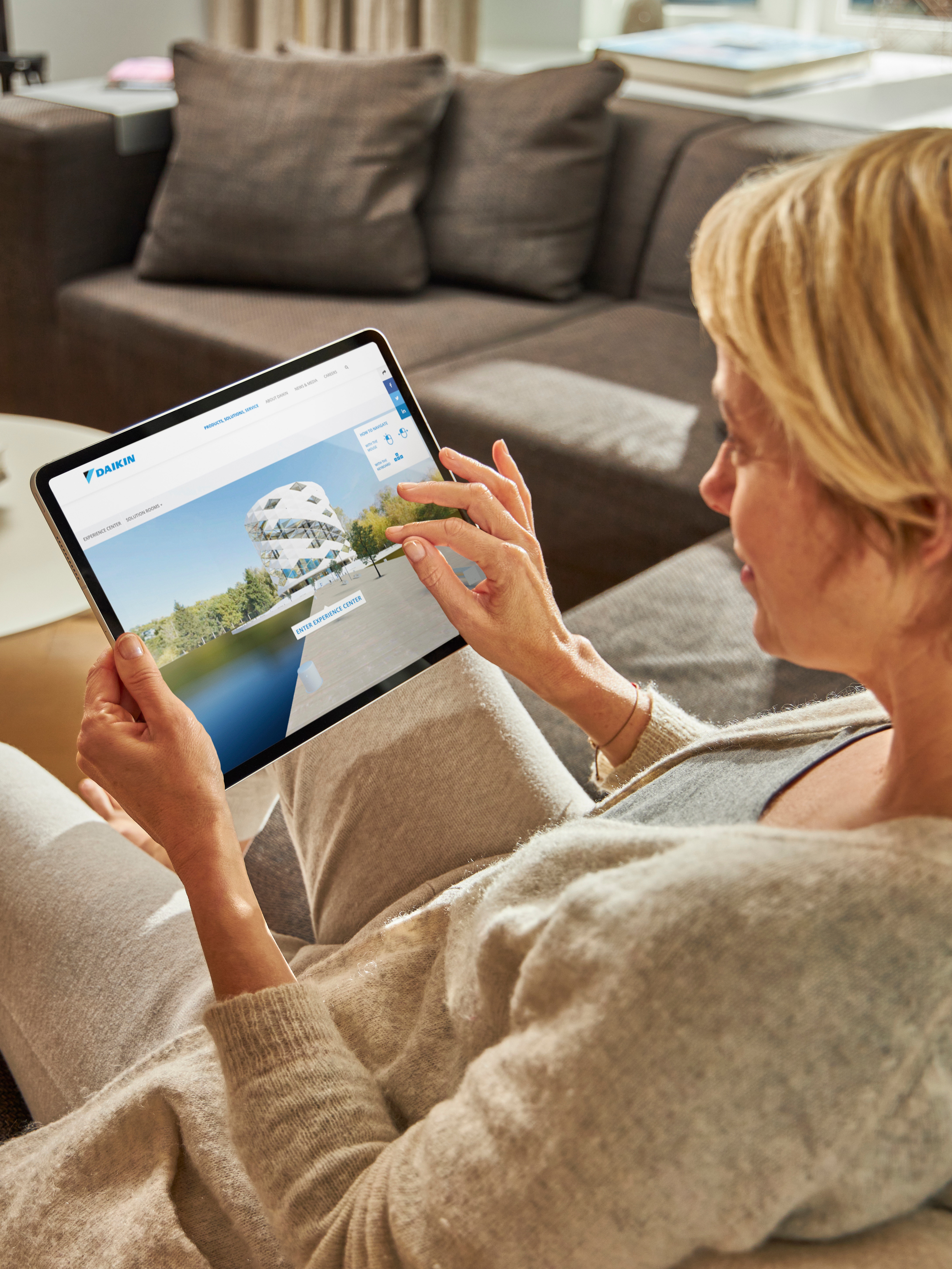 Mujer sentada en un sofá viendo los equipos de aire acondicionado en el Experience Center virtual en su tablet