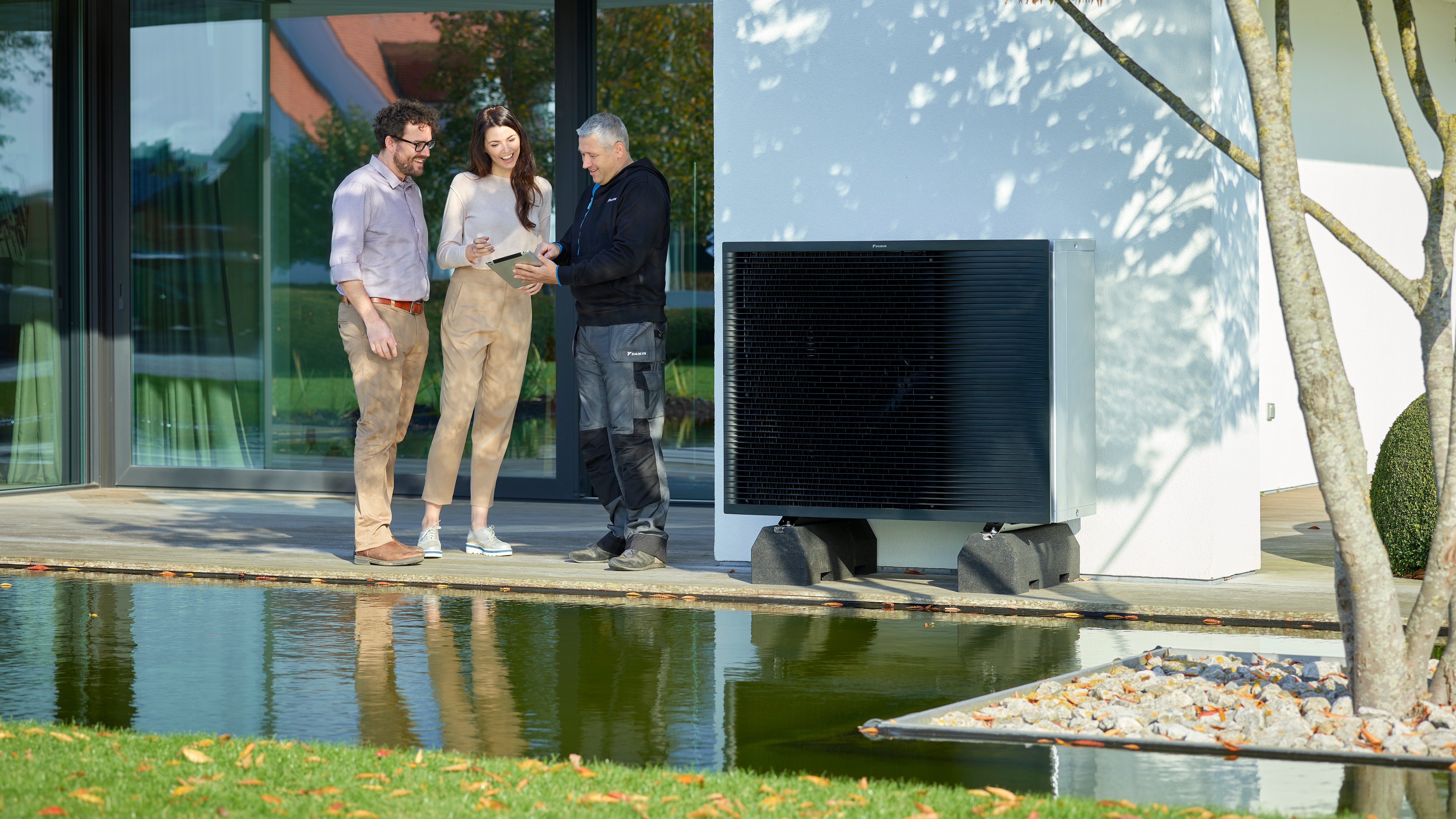 Pareja hablando con un instalador en su jardín junto a una unidad exterior Daikin Altherma