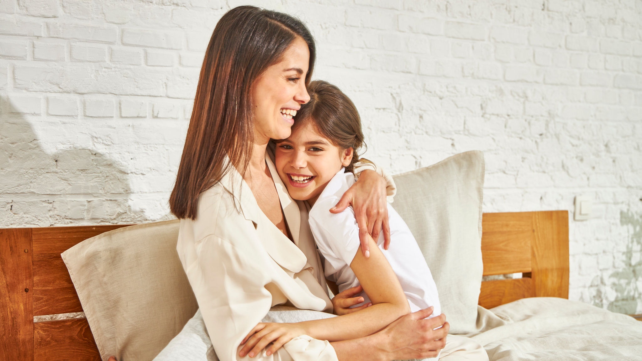 Madre abrazando a su hija y disfrutando de la temperatura en la cama