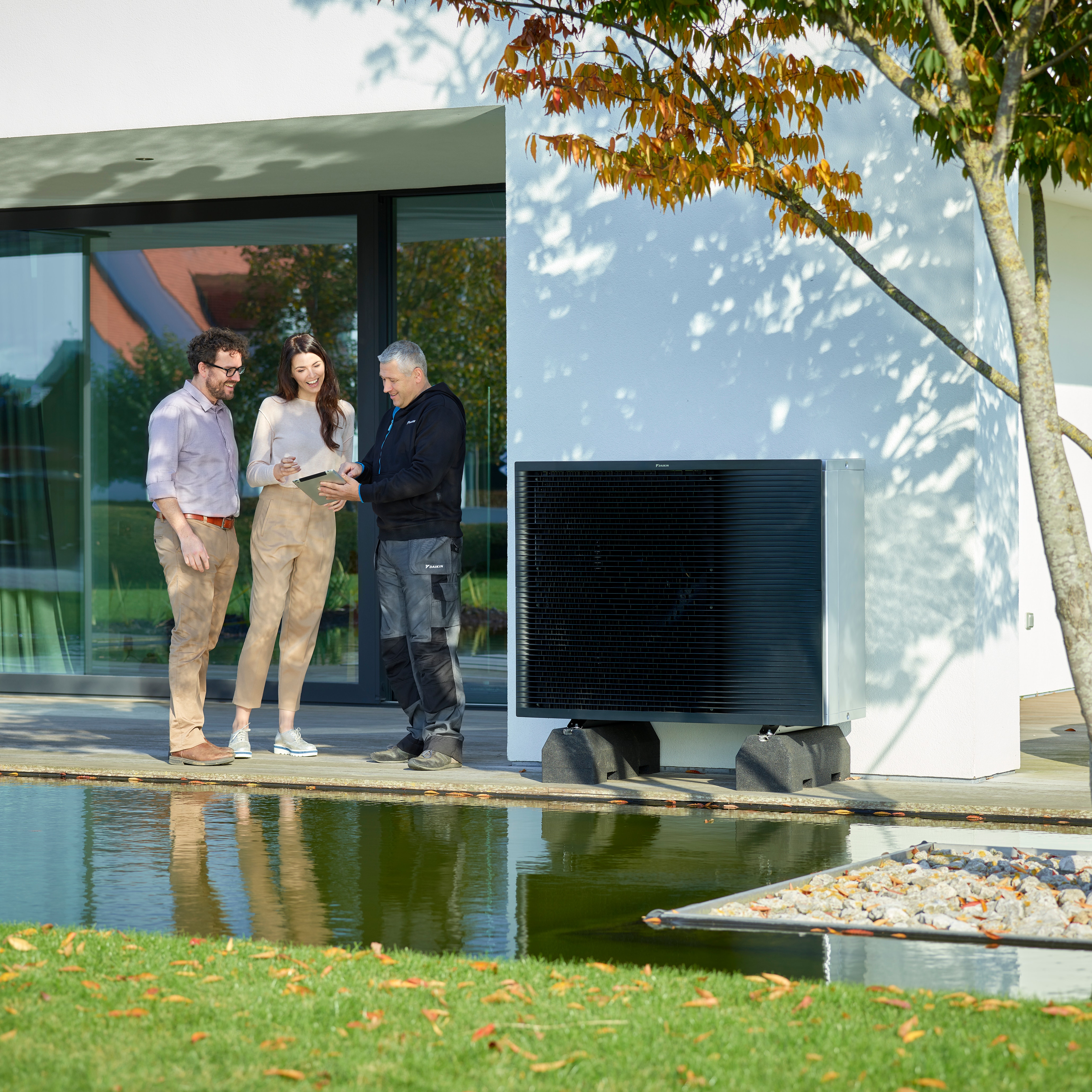 Una pareja con el instalador hablando de la instalación de un sistema de aerotermia en el exterior de su moderna vivienda